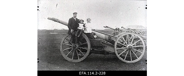 Narva mees koos kahe lapsega Joala väljal Saksa 105 mm välisuurtükil
                    istumas, taustal patarei teised suurtükid.
