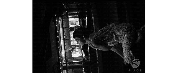 Barbara Steele in abito da sera e a piedi nudi, inginocchiata di profilo su alcuni gradini all'interno dell'Hotel Hilton; totale