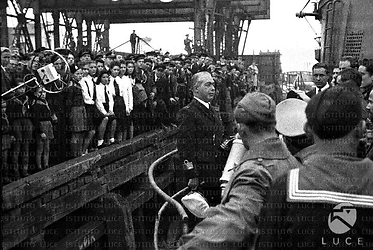 Enzo Grossi tiene discorso ai marinai schierati sul ponte del Sommergibile Barbarigo, bambini e bambine della GIL ascoltano sul molo insieme a marinai e civili