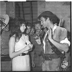 Rosanna Schiaffino e Philippe Leroy durante una pausa sul set del film Briganti italiani ; dietro delle comparse assistono alla scena - piano americano