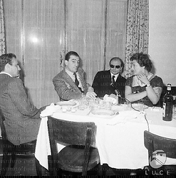 Francesco Rosi, Suso Cecchi D'Amico e Luchino Visconti e una donna conversano a tavola, durante un pranzo dei giornalisti cinematografici