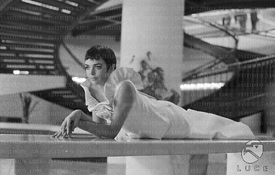 Barbara Steele in abito da sera, semidistesa su un lungo tavolo in un salone dell'Hotel Hilton. Sullo sfondo una scalinata circolare; totale
