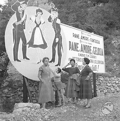 Tre donne e un bambino posano davanti al manifesto del film Pane, amore e gelosia - campo medio