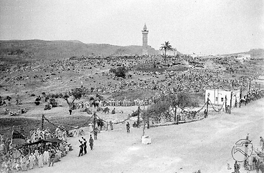 Tripoli Scorcio di un paesaggio desertico, alla periferia di Tripoli, con persone accalcate lungo la strada e sul versante di una collina; sullo sfondo svetta un minareto
