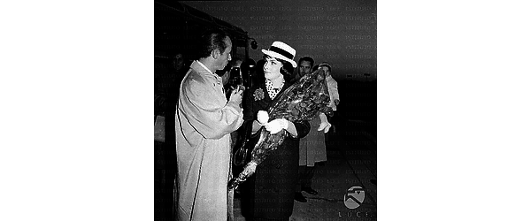 Gina Lollobrigida all'aeroporto con un mazzo di fiori uin mano conversa con Mazzarella; dietro di lei il marito con il figlio in braccio - piano americano