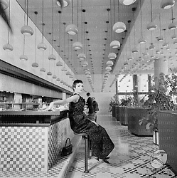 Barbara Steele, in abito da sera, seduta su uno sgabello nel bar-self service dell'Hotel Hilton. Visibile l'arredo e i lampadari del salone; campo medio