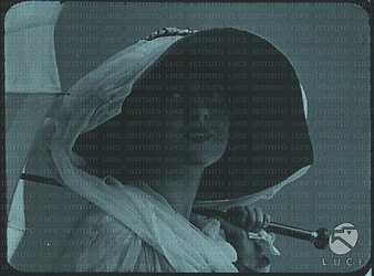 Un primo piano dell'attrice Lyda Borelli che accenna un sorriso, con un ombrello aperto appoggiato su una spalla; indossa un cappello scuro dalle ampie falde, coperto da una velina bianca