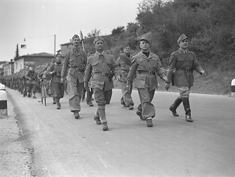 I Battaglioni della G.I.L. di Brescia sfilano lungo una strada alla periferia di un paesino guidati da tre ufficiali