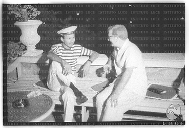Due uomini, uno in costume da marinaio, conversano seduti terrazzo di casa Roloff durante il ricevimento da lui offerto - totale