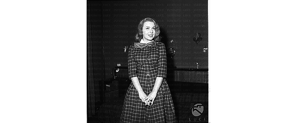 Ketty Della Porta con un vestito a quadretti e un fiocco al collo in posa in una stanza. Piano americano
