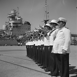 Trombettieri della Marina suonano, nave da guerra sullo sfondo
