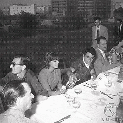 Roma Pranzo durante la pausa; tavolata sul prato con Carlo Lizzani e la troupe; Gerard Blain versa l'acqua ad Anna Maria Ferrero; sullo sfondo i palazzi di Roma