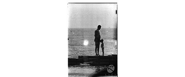 Un uomo ed un bambino in costume ripresi in piedi sul molo di Santa Marinella - campo medio
