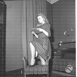 Ketty Della Porta con un piede su uno sgabello e un libro in mano. Campo medio