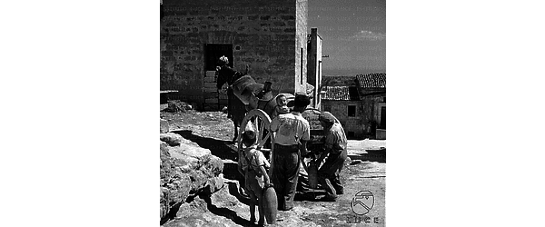 Sicilia Un uomo con bimbo in braccio, seguito da un ragazzino con un'anfora, si accosta al carretto-cisterna - deputato alla distribuzione e vendita di acqua - per provvedersi del necessario quantitativo