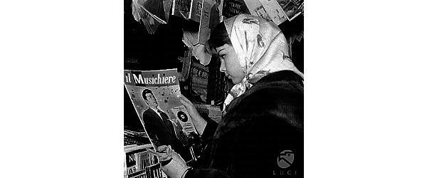 Lorella De Luca davanti all'edicola, con foulard in testa e pelliccia, osserva la foto di Toni Dallara sulla copertina del settimanale "Il Musichiere"