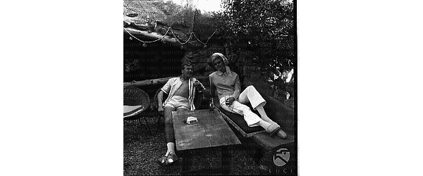 Miss Finlandia e un uomo distesi su un divano e una poltrona di vimini in una terrazza - totale