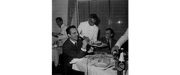 Roma Enrico Medioli parla ad un microfono seduto ad un tavolo con Luchino Visconti durante un pranzo dei giornalisti cinematografici