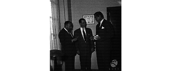 Tre uomini in piedi in un ufficio sorridono, forse ad uno dei tre viene conferita un'onorificenza; piano americano
