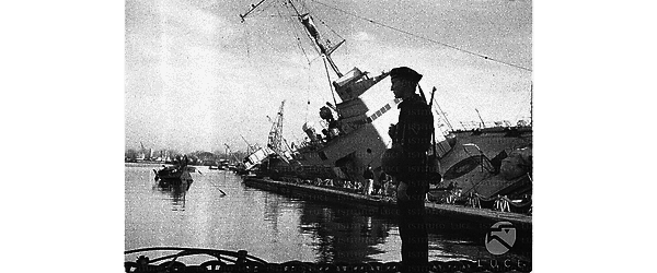 Marinaio tedesco di guardia su un molo del porto di Tolone, sullo sfondo una nave da guerra francese danneggiata e inclinata su un lato