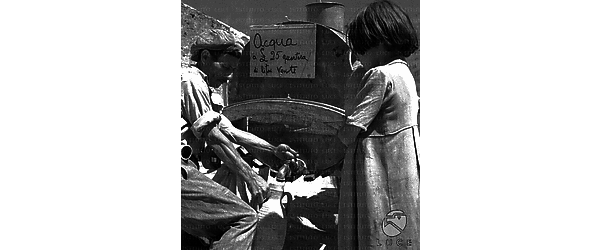 Sicilia Una bambina, in piedi vicino al carretto-cisterna itinerante nella provincia del trapanese, osserva l'acquaiolo riempirle l'anfora con l'acqua prelevata dal carretto