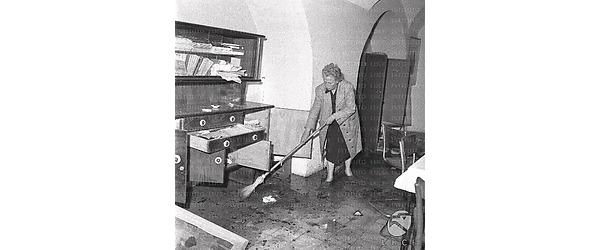 Interno devastato del Circolo Culturale: una donna spazza il pavimento allagato, davanti ad un mobile con cassetti e sportelli manomessi, Campo medio