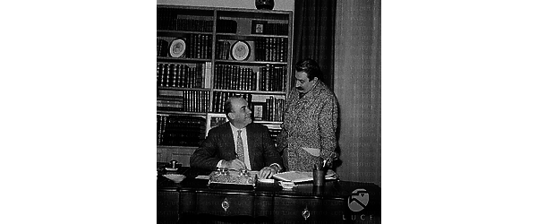 Guareschi in piedi accanto ad un uomo seduto davanti ad un'imponente scrivania di legno, probabilmente si tratta del produttore Gastone Ferranti.