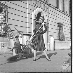 Una modella con un vestito elegante posa davanti a due  bidoni della spazzatura con una scopa in mano, Campo medio