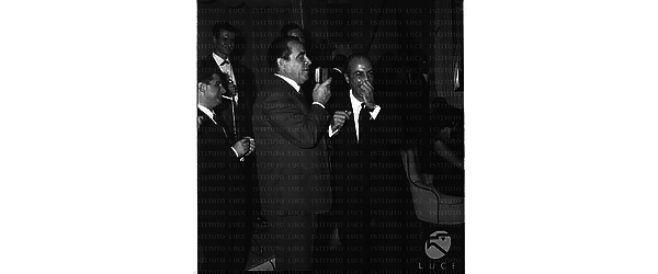 Carlo Dapporto parla al microfono, accanto a lui Silvio Noto in un locale romano - piano americano