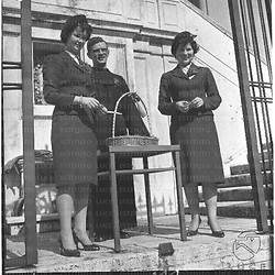 Un sacerdote e due donne davanti alla Chiesa di Sant'Isidoro, con un cestino su un piccolo tavolo - totale