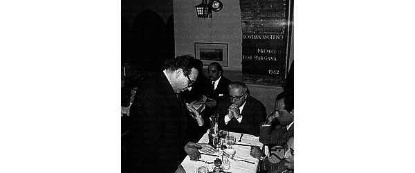 Un uomo in piedi, Biagi e Piccioni seduti al tavolo