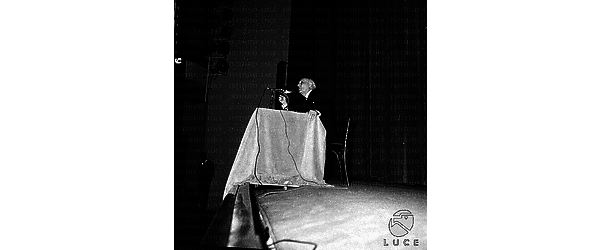 Della Torre tiene la sua conferenza seduto ad un tavolino con microfono sul palco di un teatro
