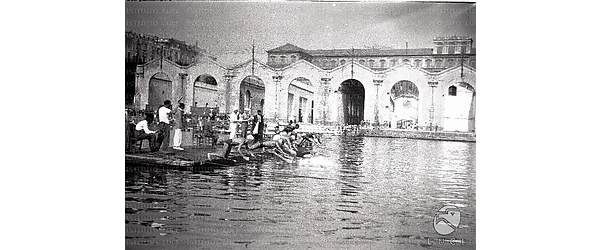 Napoli Scorcio del molo dal quale si stanno tuffando i nuotatori, sullo sfondo di antiche strutture in disuso
