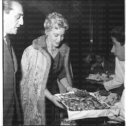 Maria Schell e Visconti davanti a un vassoio di stuzzichini durante un rinfresco. Piano americano