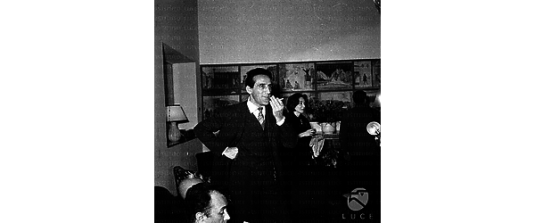 Arnoldo Foà fuma una sigaretta in sala, alle sue spalle altri ospiti del convegno