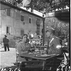 Roberto Risso, vestito da carabiniere, e un'attrice - la Merlini (?) -, seduti al tavolo di un bar all'aperto durante le prove del film "Pane, amore e gelosia" (?).
