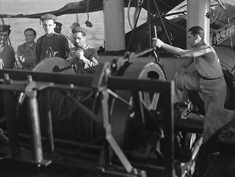 Marinai manovrano un argano sul ponte dell'imbarcazione con vele e motori