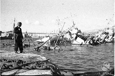 Navi da guerra francesi semi-affondate nelle acque del porto di Tolone, un marinaio tedesco armato di fucile sta di guardia sul molo