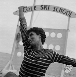 Rita Gam in posa sul molo in legno, alle sue spalle un'insegna con la scritta: Ecole ski school; piano medio