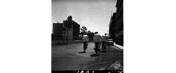 Poliziotti in bicicletta ripresi di spalle in una via romana di periferia - campo medio