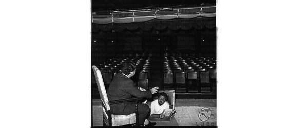 Tony Caccialupo seduto su una poltrona sul palco del teatro Lo Chalet. Oscar Boscaro nella buca del suggeritore - campo medio