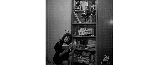 Ludovica Modugno legge un libro accovacciata vicino ad una libreria; totale