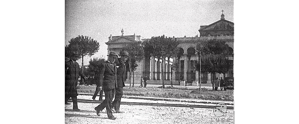 Roma Benito Mussolini, insieme al principe Boncompagni Ludovisi e altre persone, passeggia per un'area sterrata, davanti alla basilica di San Paolo Fuori le Mura a Roma