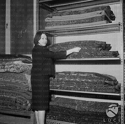 Franca Tamantini, in un laboratorio, sistema alcuni tappeti ripiegati; totale