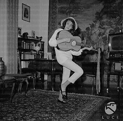 Ludovica Modugno suona la chitarra in piedi al centro di un salotto; totale