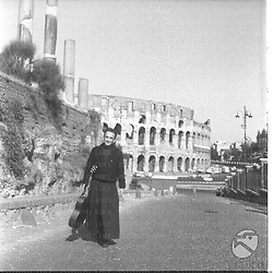 Il gesuita francese Padre Aimé Duval ripreso mentre cammina con la chitarra di lato ed il Colosseo sullo sfondo - campo medio