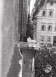 Roma Benito Mussolini, ripreso di profilo, sorridente, è affacciato al balcone di Palazzo Venezia a Roma, e sta arringando la folla sottostante