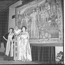Il cantante Nicola Rossi Lemeni con due donne sotto un telo raffigurante un sovrano mitologico con in mano uno scettro. Campo medio