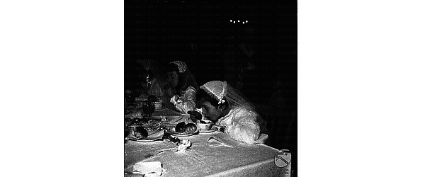 Bambine con abito della comunione mangiano sedute ad un tavolo - piano americano