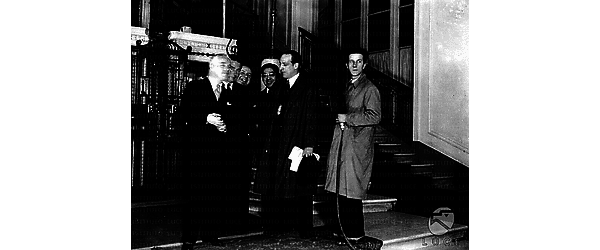 Roma Charlie Chaplin colto con alcune persone vicino all'ascensore dell'albergo; un uomo sulla destra ha in mano un microfono